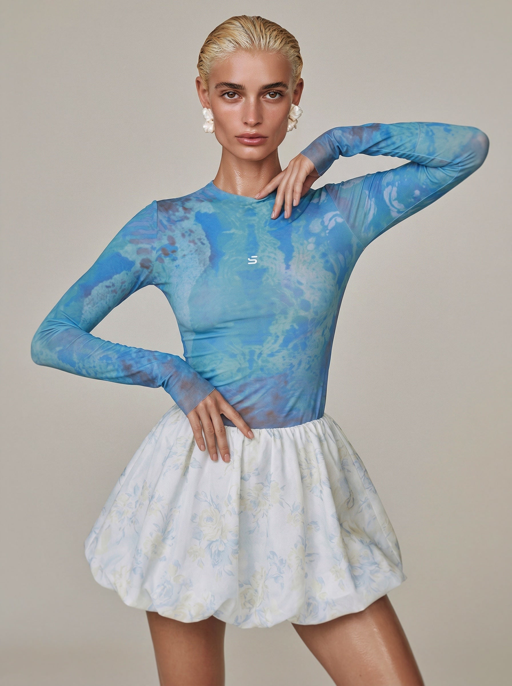 Woman wearing a blue long-sleeve top and white skirt against a neutral background