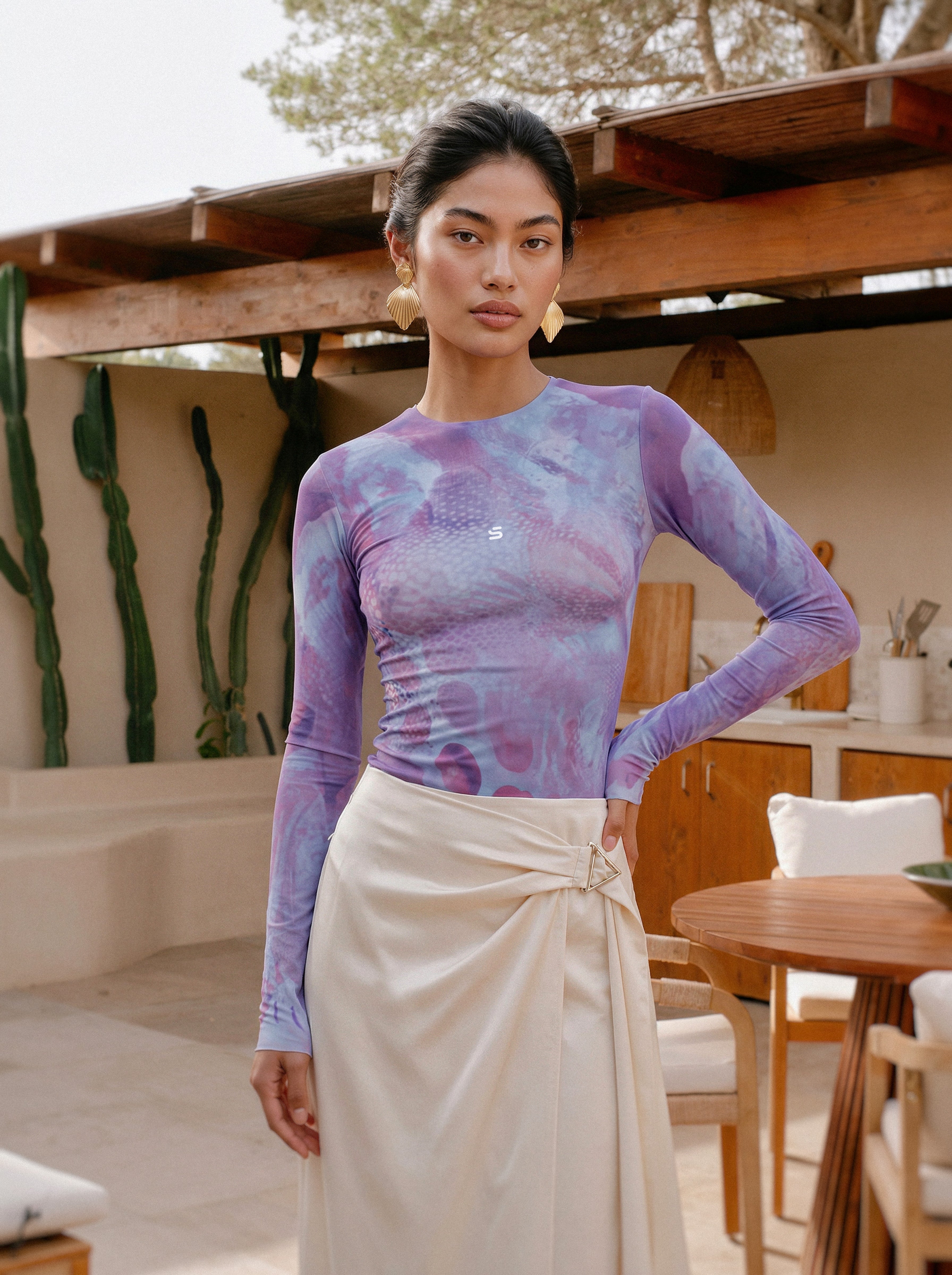 Woman wearing a patterned purple top and beige skirt in an outdoor setting.