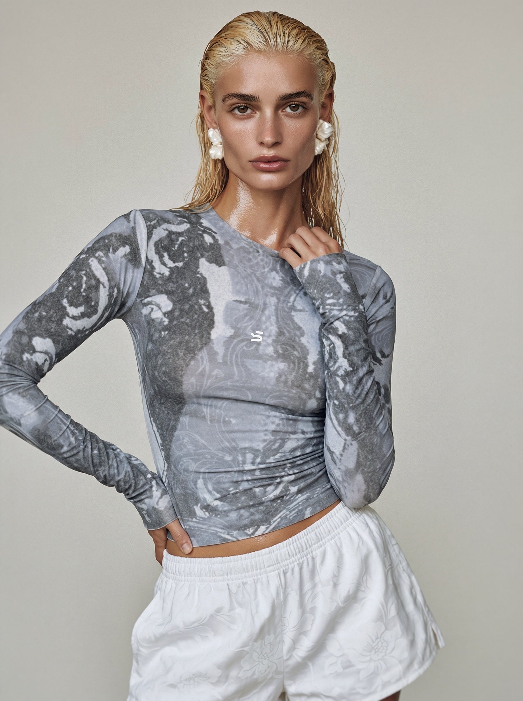 Woman wearing a gray long-sleeve athletic top with a subtle pattern and white shorts on a plain background.