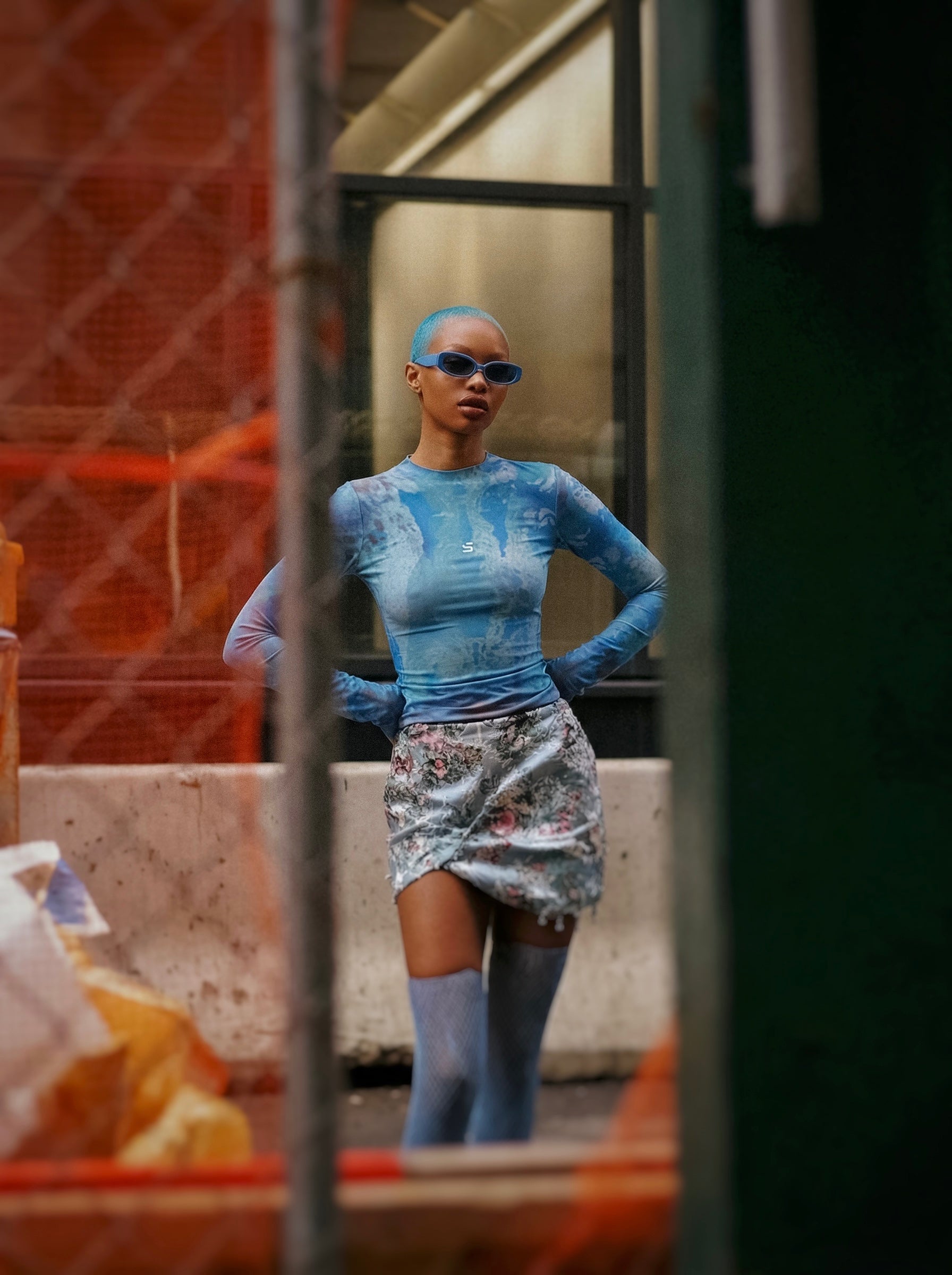Person wearing a blue longsleeve top with floral skirt in an urban setting