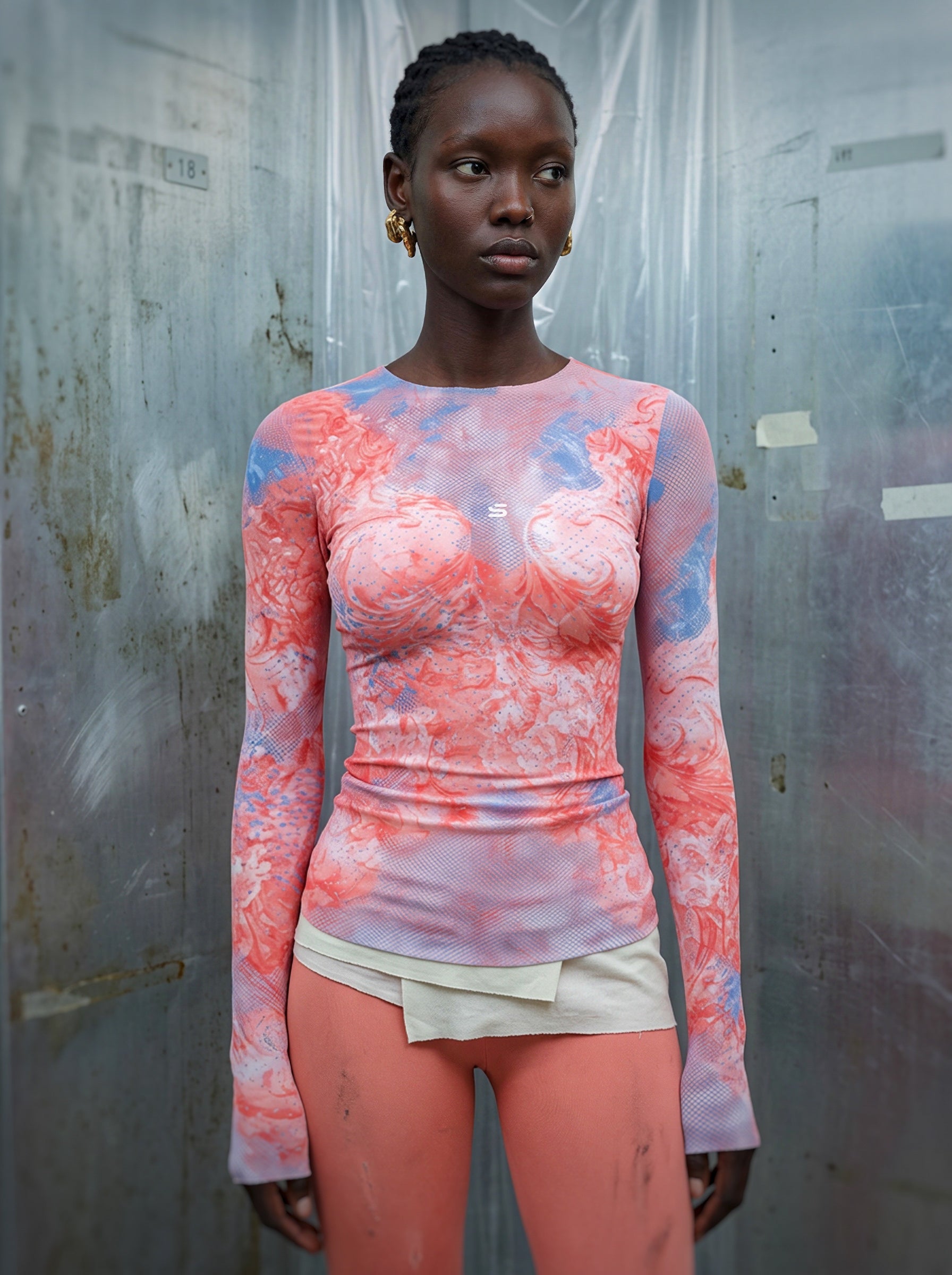 Model wearing a colorful long-sleeve top and shorts against a textured wall.