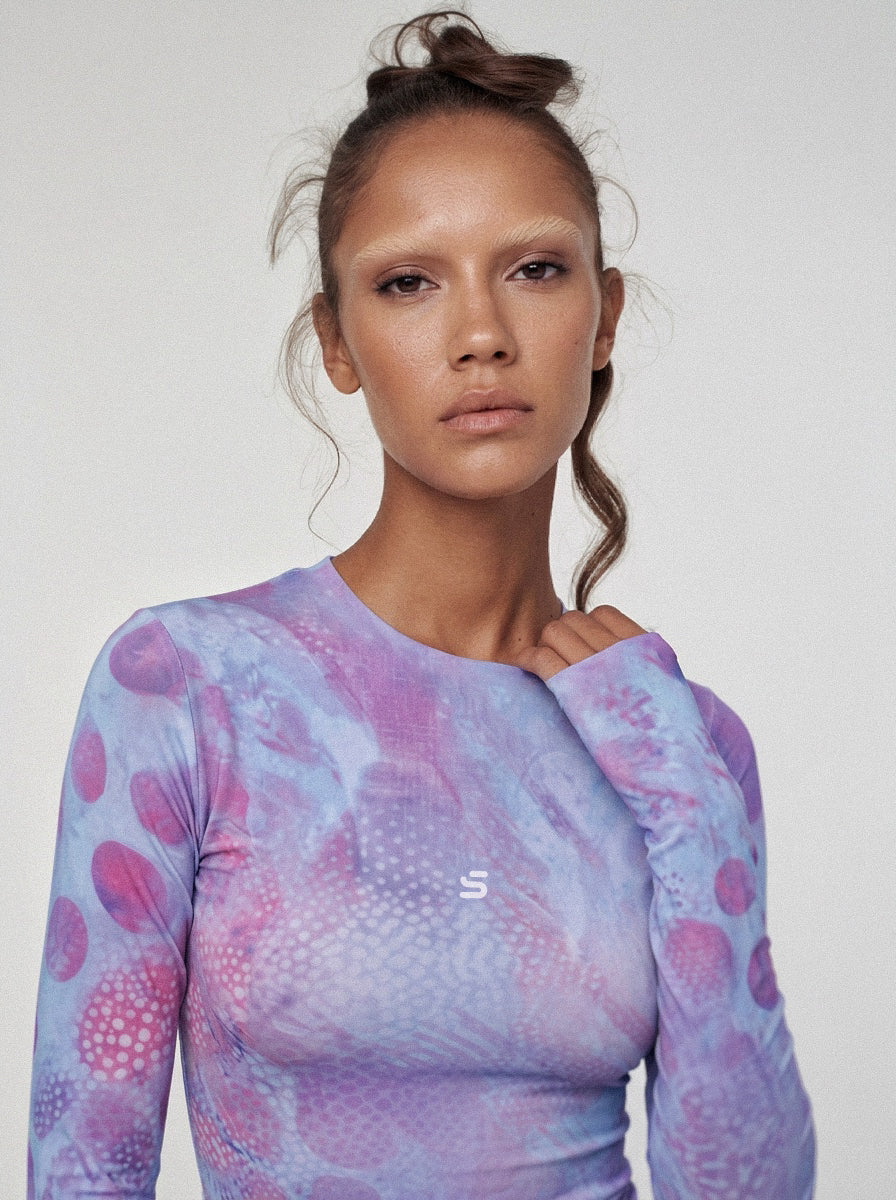 Woman wearing a long-sleeve, patterned top with a plain background