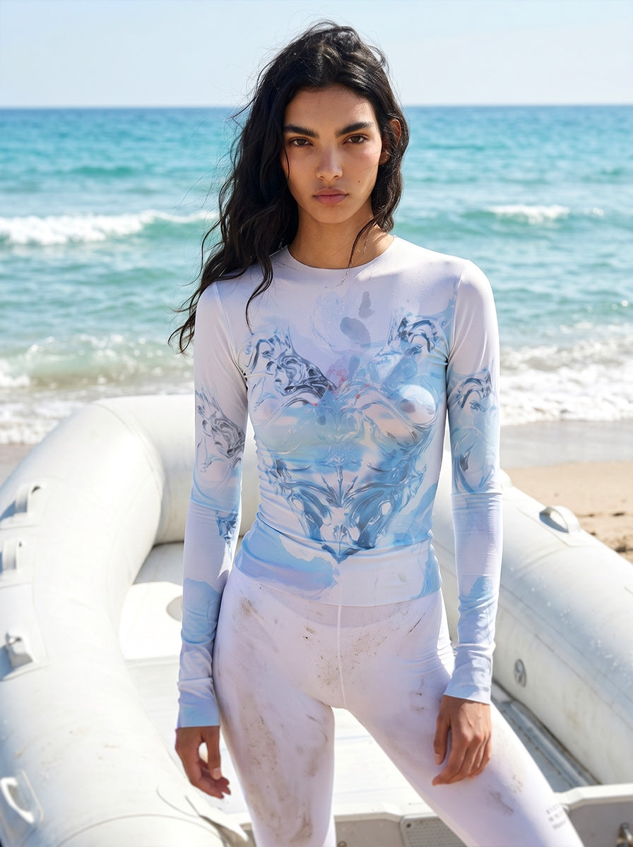 Woman wearing a white and blue patterned long-sleeve top and pants on a beach.